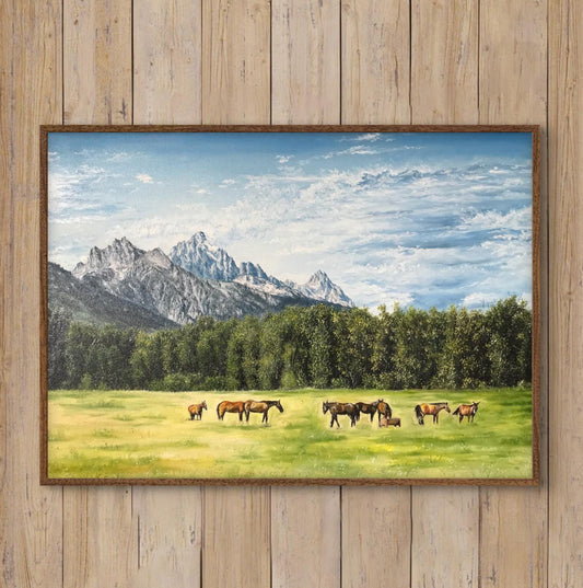 Framed landscape painting of horses in a field with mountains, displayed on a wooden wall above a white armchair.