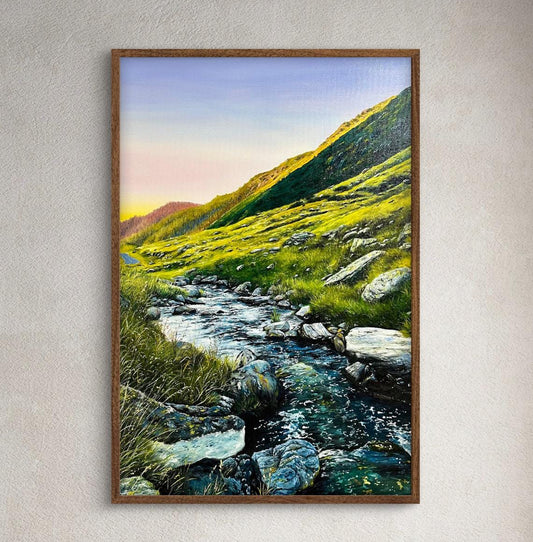 Framed landscape painting of a mountain stream on a wall in a room with wooden furniture and decor.