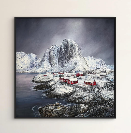 Framed artwork of a mountainous landscape with red structures on a white wall.
